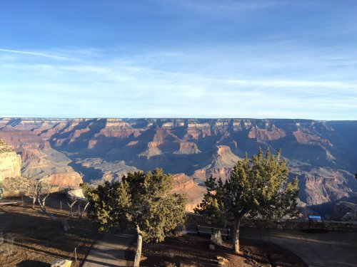 A panoramic view of the Grand Canyon, showcasing layered rock formations and a clear blue sky.