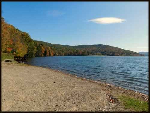 A serene lakeside view with colorful autumn trees and a clear blue sky, reflecting on calm water.