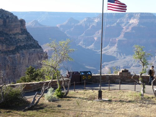 A scenic view of the Grand Canyon with a flagpole and a visitor near the edge, showcasing the canyon's vast landscape.