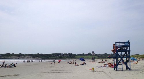 A sandy beach with sunbathers, umbrellas, and a lifeguard tower, under a cloudy sky.