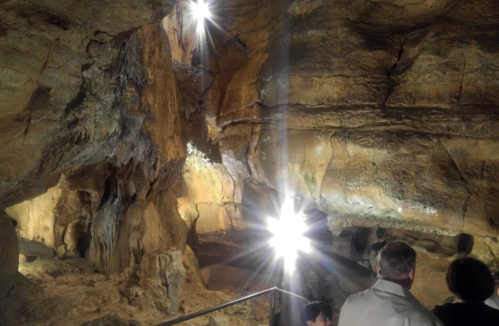 Visitors explore a dimly lit cave, illuminated by bright lights reflecting off the rocky walls.