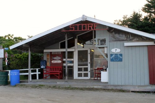 A small, rustic store with a red "STORE" sign, benches outside, and a gravel path leading up to the entrance.