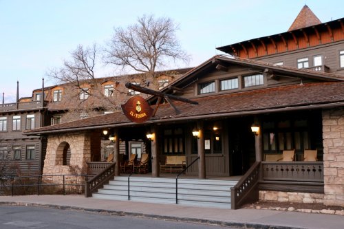 A rustic building with a wooden sign, featuring a porch and large windows, set against a twilight sky.