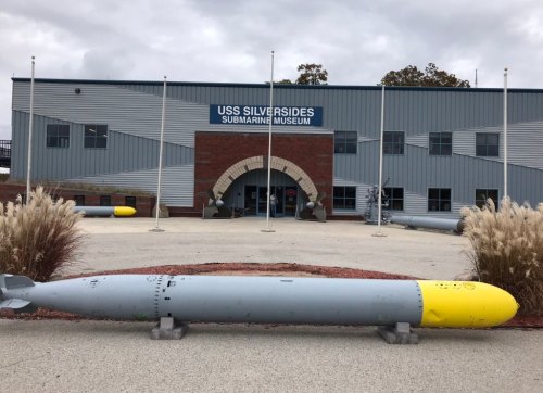 Exterior of the USS Silversides Submarine Museum, featuring a large torpedo in front and flags on display.