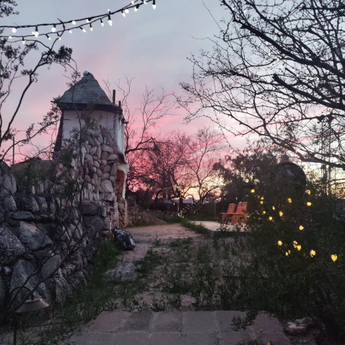 A serene landscape at sunset, featuring a stone structure, bare trees, and string lights illuminating the path.