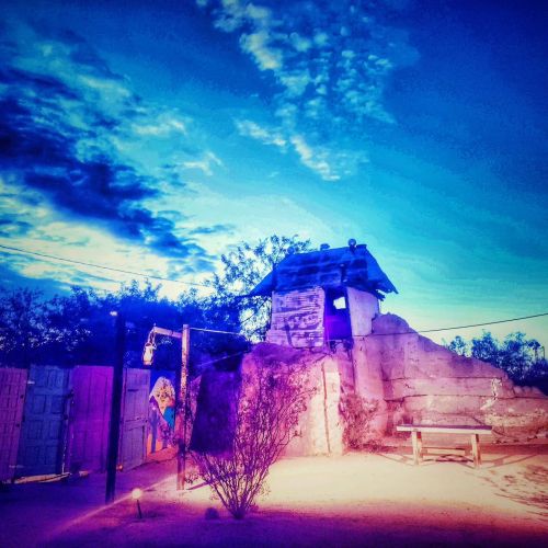 A rustic structure atop a hill under a vibrant blue sky, surrounded by sparse vegetation and a tranquil atmosphere.