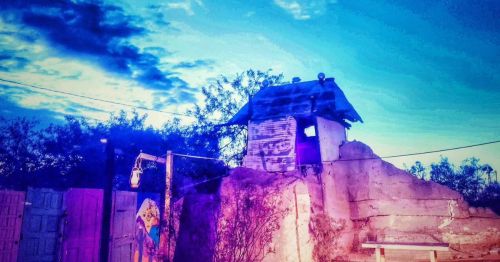 A small, rustic structure atop a rocky formation under a vibrant twilight sky with scattered clouds.