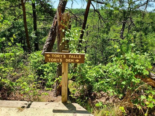 Wooden signpost pointing to Tory's Falls and Tory's Den, surrounded by lush greenery and trees.