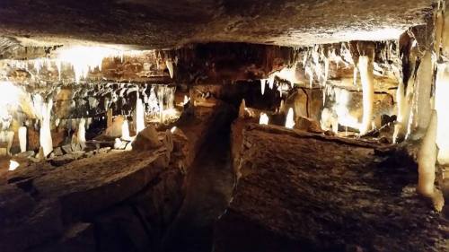 A dimly lit cave with stalactites and stalagmites, featuring glowing lights along a winding path.