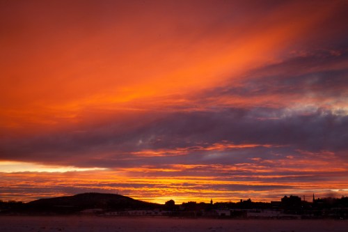 Vibrant sunset with orange and purple hues over a silhouette of hills and buildings.