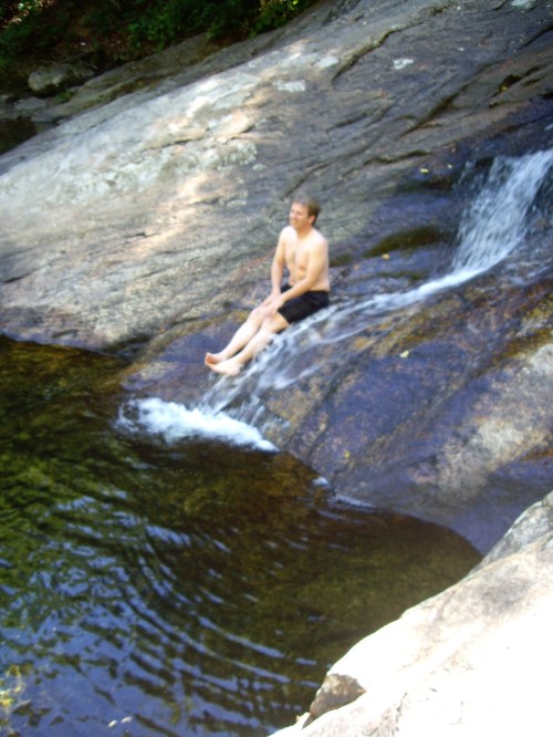 A person sitting on a rock by a small waterfall, enjoying the water in a natural setting.