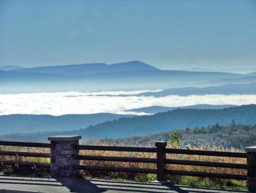 A scenic view of mountains shrouded in mist, with a clear blue sky above and a wooden railing in the foreground.