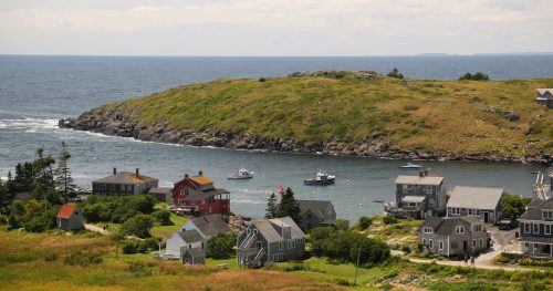 A coastal scene featuring colorful houses, boats in the water, and a green hillside under a cloudy sky.