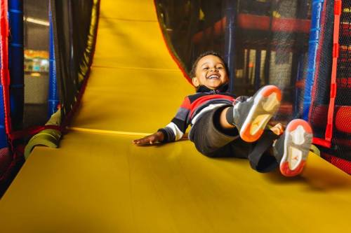 A joyful child slides down a bright yellow slide in a play area, smiling as they enjoy the fun.