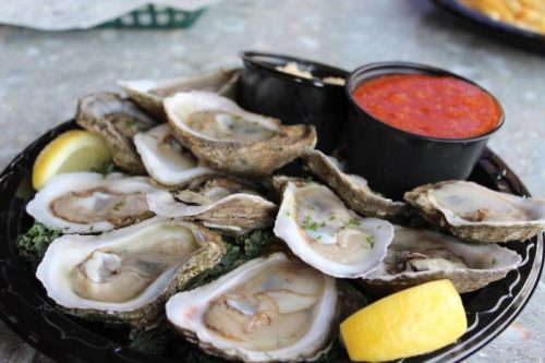 A platter of fresh oysters on the half shell, served with lemon wedges and dipping sauces.