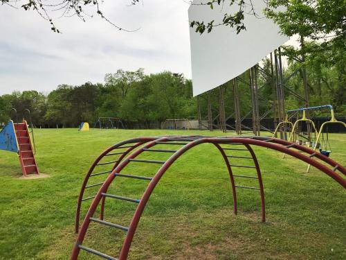 A playground with climbing structures and swings, set in a grassy area with trees in the background.