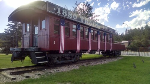 A vintage red train car on tracks, decorated with American flags, set against a blue sky and green grass.