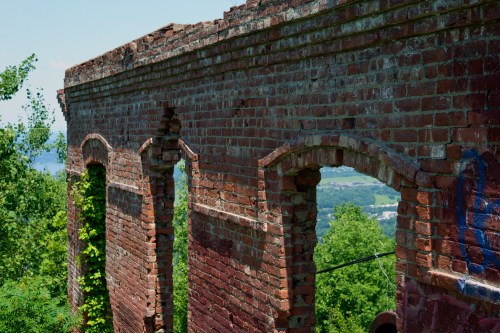 Weathered brick ruins with arched openings, surrounded by greenery and overlooking a scenic landscape.