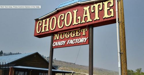 Sign for "Chocolate Nugget Candy Factory" with a rustic design, set against a mountainous backdrop.