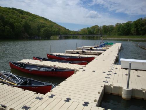 A serene lake scene with red canoes docked at a wooden pier, surrounded by green trees and a cloudy sky.