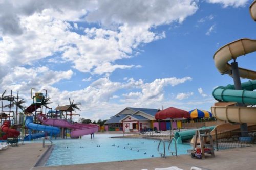 A vibrant water park featuring colorful slides, a pool, and a cloudy blue sky in the background.