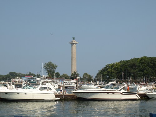 A marina filled with boats, featuring a tall monument in the background against a clear blue sky.