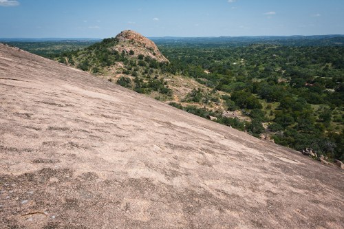 A vast landscape featuring a rocky hill surrounded by lush greenery under a clear blue sky.