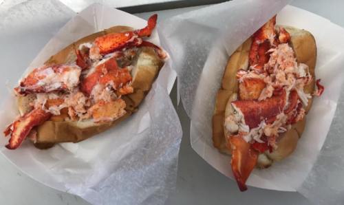 Two lobster rolls filled with chunks of lobster meat, served in soft, toasted buns and wrapped in white paper.