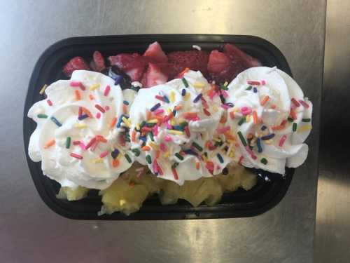 A dessert bowl with whipped cream, colorful sprinkles, strawberries, and pineapple chunks.