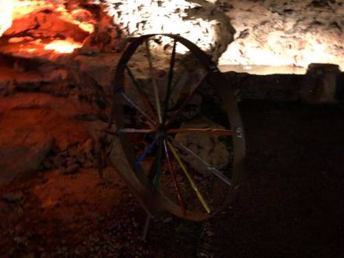 A colorful wheel with multiple spokes, set against a rocky, illuminated background.