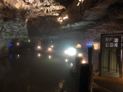 A dimly lit cave interior with water, illuminated by colorful lights and reflections on the surface.
