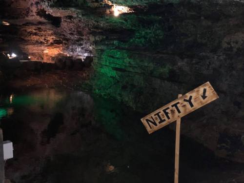 A dimly lit cave with a wooden sign pointing downwards, indicating "Nifty," next to a still body of water.