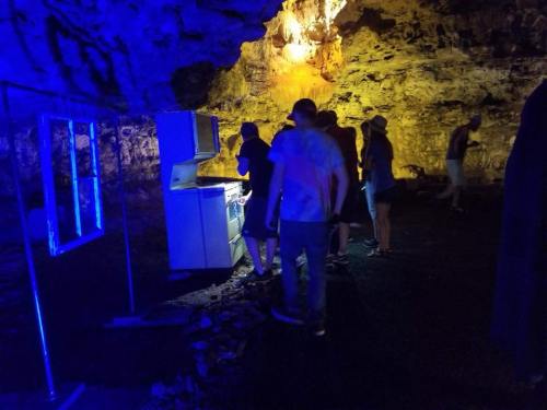 A group of people exploring a cave with blue lighting, near a white refrigerator and rocky walls.