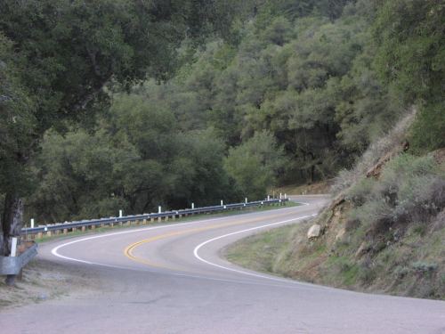 A winding road curves through a lush green landscape, surrounded by trees and hills.
