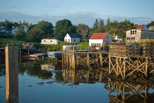 A serene waterfront scene with boats, wooden docks, and colorful houses reflecting in calm water.