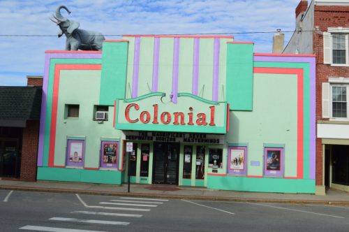 Colorful Colonial theater building with a large elephant statue on the roof, featuring bold stripes and signage.