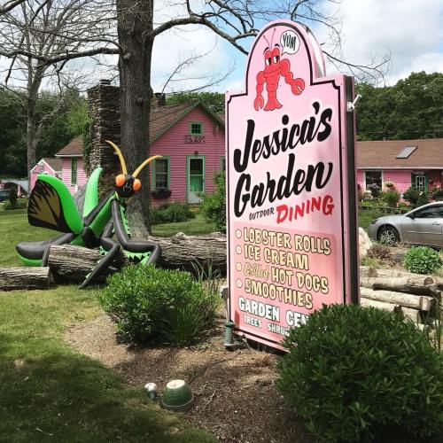 A colorful restaurant sign for "Jessica's Garden" with a large insect sculpture outside, surrounded by greenery.