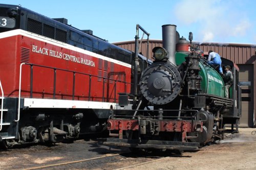 A vintage steam locomotive in green next to a red diesel engine at the Black Hills Central Railroad.