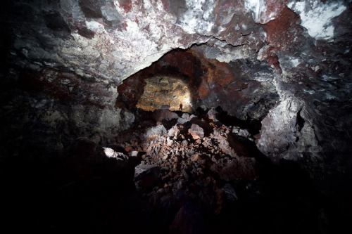 A dark cave interior with rocky formations and a small figure illuminated by a flashlight in the distance.