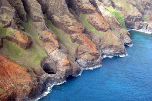 Aerial view of rugged coastal cliffs with green vegetation and blue ocean waves below.