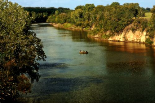 A serene river scene with a small boat and lush greenery along the banks under a clear blue sky.