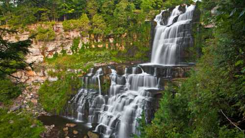 A stunning waterfall cascading down rocky cliffs, surrounded by lush green foliage and trees.