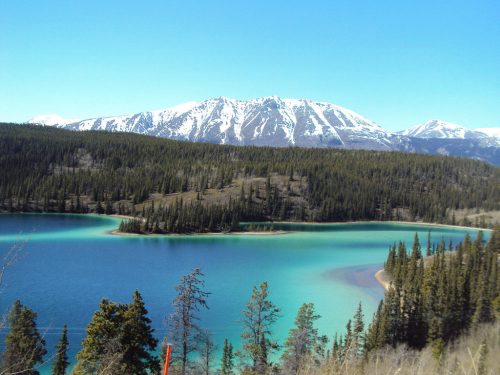 A serene lake surrounded by lush forests and snow-capped mountains under a clear blue sky.