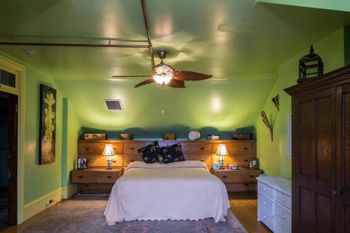 Cozy bedroom with green walls, a ceiling fan, a bed with a light blanket, and wooden furniture. Soft lighting creates a warm atmosphere.