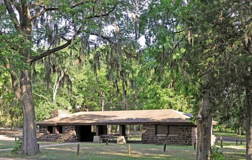 A rustic stone building surrounded by lush green trees and hanging moss in a serene outdoor setting.