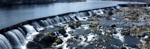 A scenic view of a river with cascading waterfalls over rocky terrain, surrounded by trees and a clear sky.