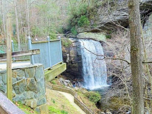 A serene waterfall cascades down rocky cliffs, surrounded by trees and a wooden viewing platform.