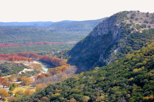 A scenic view of rolling hills and a river, surrounded by trees with autumn foliage in vibrant colors.