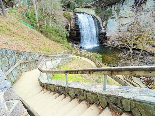 A scenic view of a waterfall surrounded by greenery, with stone steps leading down to the water's edge.