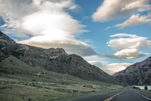 A scenic view of a winding road surrounded by mountains and dramatic clouds under a blue sky.